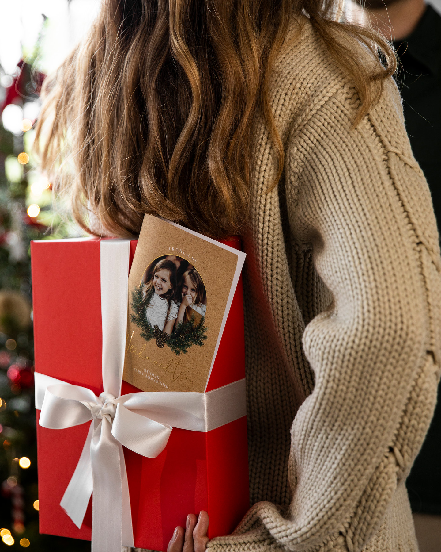 Mädchen hält Geschenk mit Weihnachtskarte hinterm Rücken