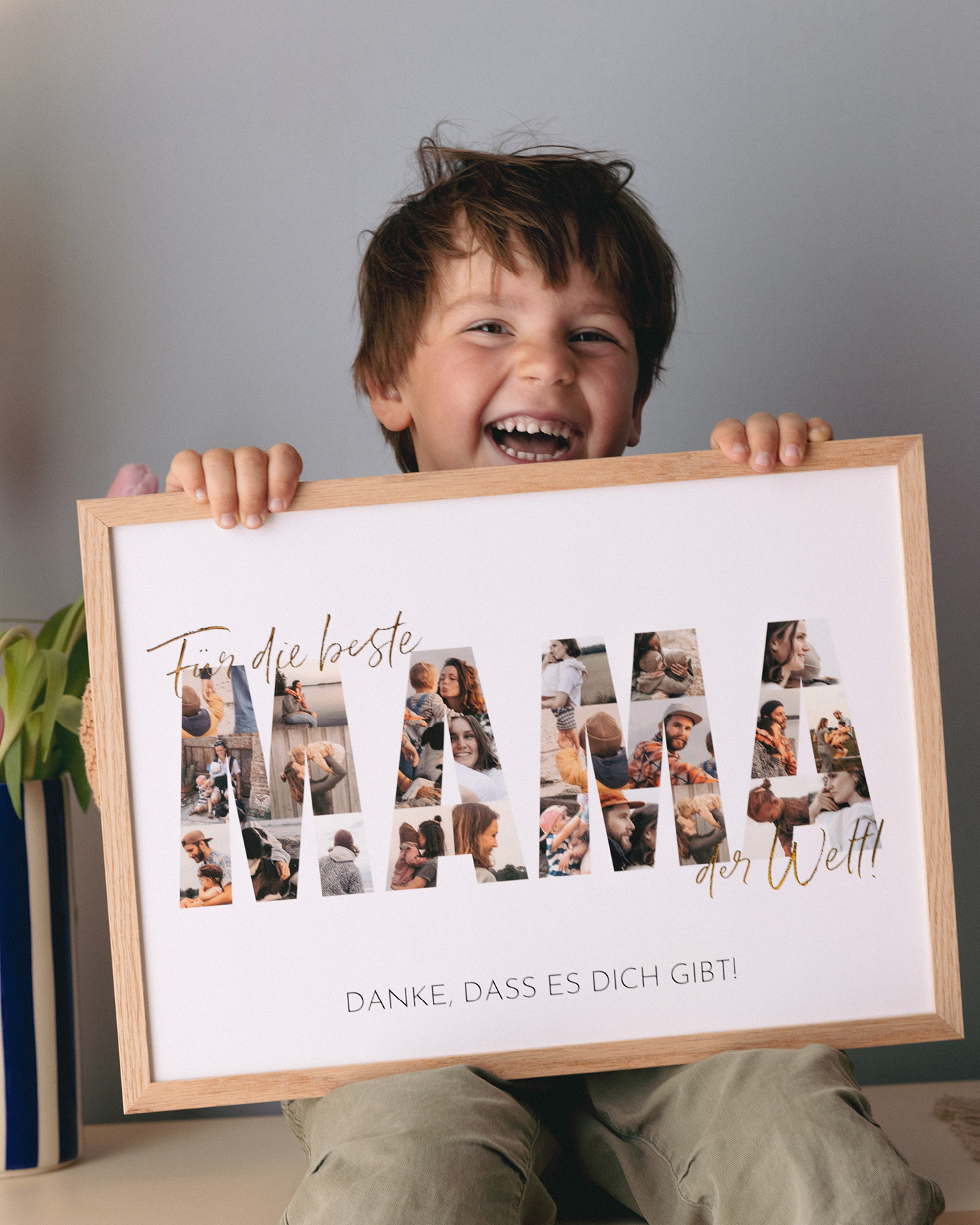 Lachender kleiner Junge hält eine gerahmte Collage mit dem Schriftzug "Mama" zum Muttertag