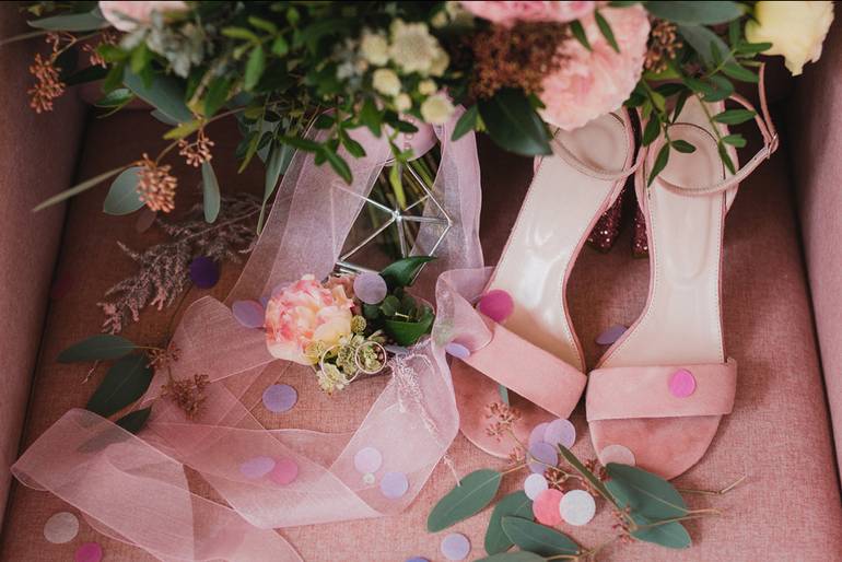 Pinkfarbene Sandaletten und Brautstrauß mit rosa Schleife, dekoriert mit Konfett und Blättern