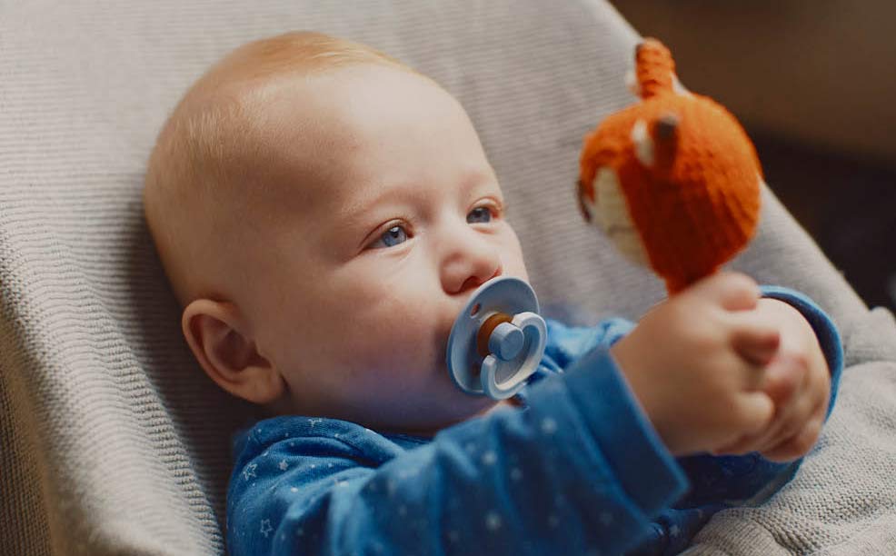 Baby hält Babyspielzeug in der Hand und betrachtet die Rassel genau