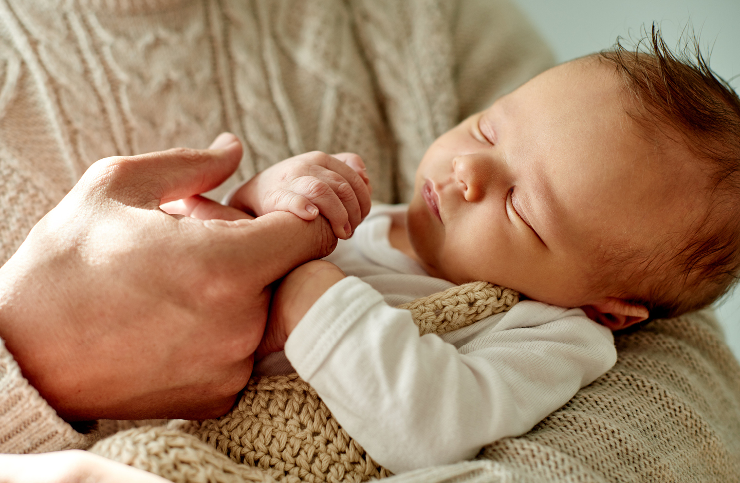 Schlafendes Baby im Arm des Vaters umfasst mit einer Hand dessen Zeigefinger