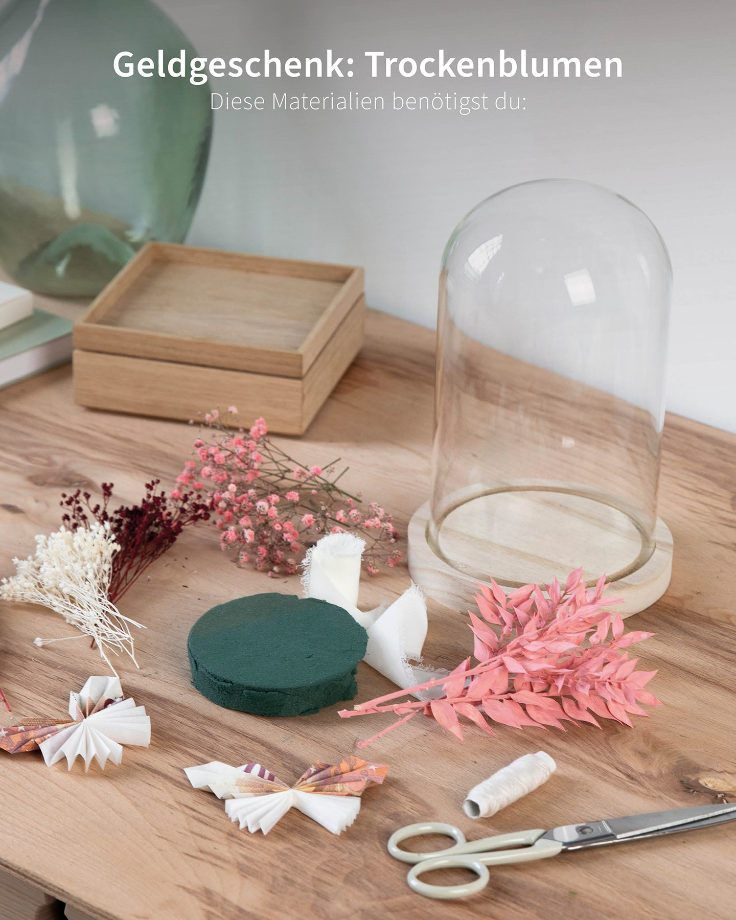 Materialien auf dem Tisch liegend. Glaskuppel mit Trockenblumen und Schmetterlingen aus Geld. 