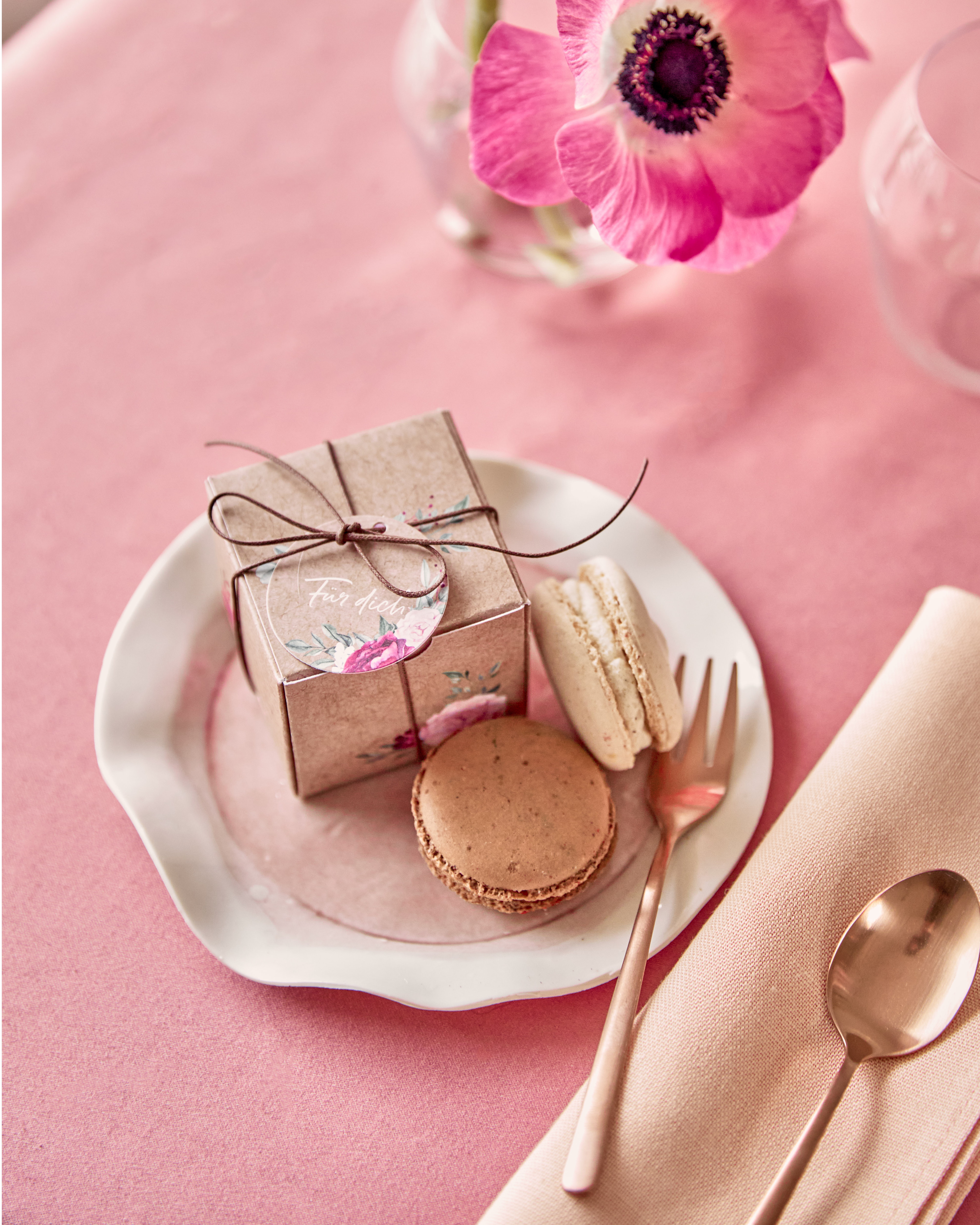 Gastgeschenkbox im Kraftpapierlook mit Blumendesign auf einem Teller mit Macarons